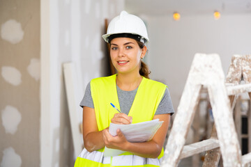 Young woman builder holding documents, smiling and looking at camera. Repair works in house.