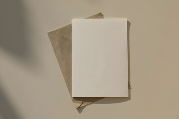 Empty greeting card, invitation mockup, craft envelope in sunlight, beige table background. Long...