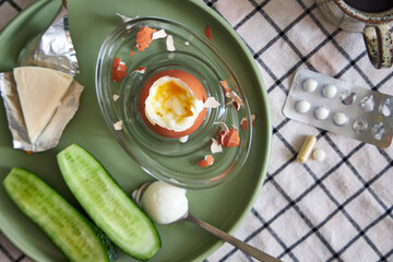Top view of a breakfast on the table with a boiled egg, coffee, a glass of water, and pills
