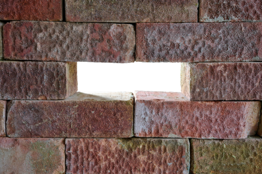 An old, textured brick wall with a transparent opening where a brick is missing. 