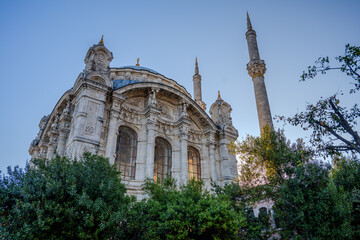 Low Angle View of Ornate Facade and Minarets of the Historic Ortaköy Mosque Framed by Greenery in...