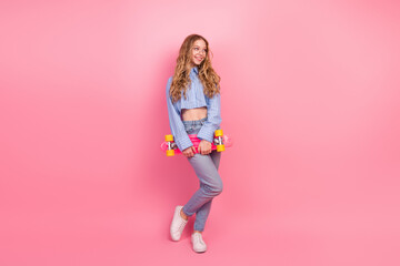 Charming young woman in casual striped shirt holding an orange and pink skateboard against a...