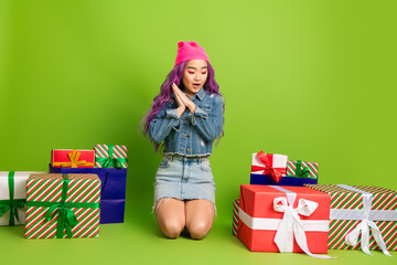 Young woman with purple hair surrounded by colorful holiday gift boxes on a green background...