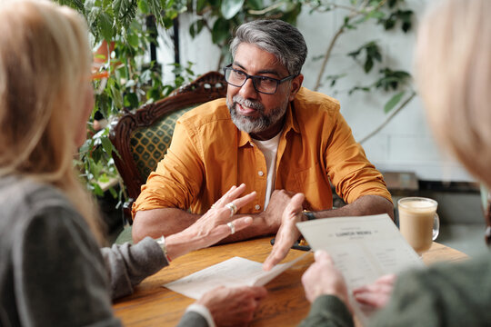 Asian senior man engaging in conversation with colleagues around table, sharing business ideas and documents, focusing on developing strategies for future success