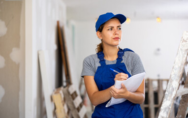 Woman in blue overalls checking completed construction work on the drawing