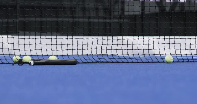 Padel tennis indoor court with balls and racket resting against net on blue surface, copy space