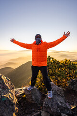 Adventurer in bright orange jacket embracing mountain sunrise