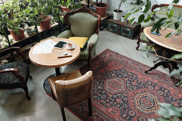 Inviting cafe setting featuring vintage furniture, a patterned rug, and numerous potted plants....