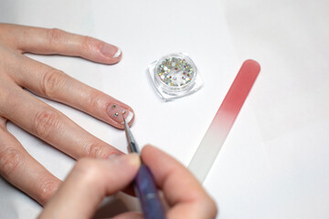 A woman is doing a manicure, fixing diamond rhinestones on her nails.