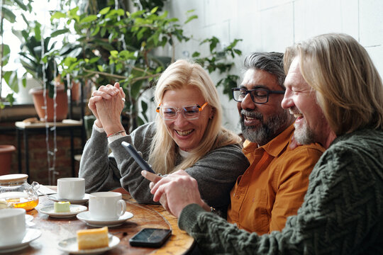 Group of friends enjoying coffee and cake while chatting and sharing laughter in a cozy cafe setting with plant decor and natural light