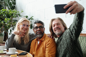 Friends from different backgrounds smiling while posing for selfie during casual meetup at cozy cafe, capturing moment of joy and friendship