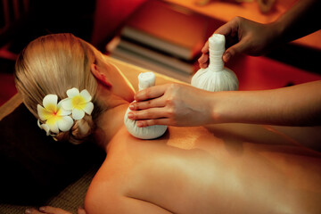 Hot herbal ball spa massage body treatment, masseur gently compresses herb bag on woman body....