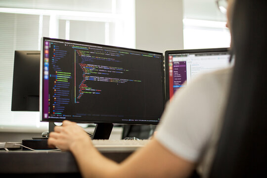 Woman coding on dual monitor setup in modern office