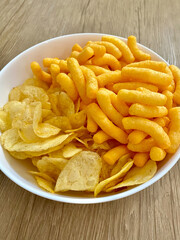 Snack bowl filled with crispy potato chips and cheese puffs on wooden table ready for sharing