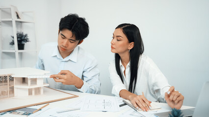 Obraz premium Professional male engineer measure house model by using ruler while beautiful cooperative coworker working together by using laptop to analysis data. Creative design and teamwork. Closeup. Immaculate.