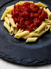 Penne pasta with in red sauce on a stone plate, stone or concrete background