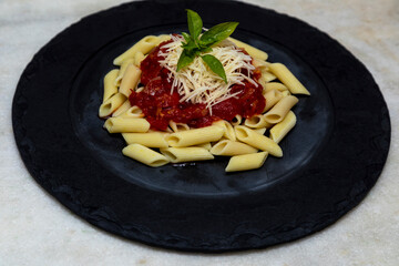 Penne pasta with red sauce and parmesan cheese on a black plate.  Stone or concrete background