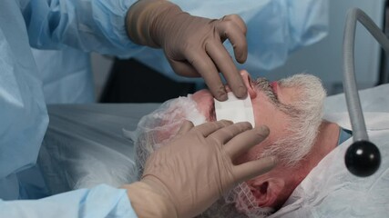 Closeup of gloved medical professional gently applying protective eye patch to senior male patient after ophthalmic surgery, ensuring proper postoperative care and hygiene - Powered by Adobe