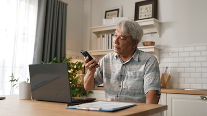 Stressed senior manager talking to colleague by using smart phone and planning marketing strategy. Businessman checking report and calling colleague while sitting at home. Remote working. Myrmidon.