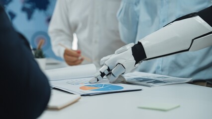A robotic hand points to a business chart during a collaborative meeting in a modern office,...