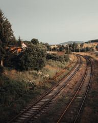 Curved railway tracks leading through an idyllic, rural landscape with lush vegetation and hills in...