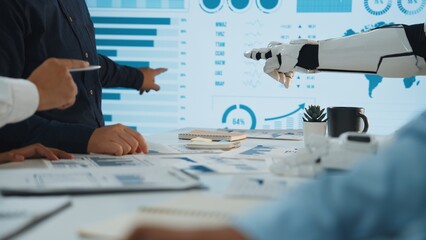 A collaborative meeting scene showcasing human hands and a robotic arm interacting with visual data, symbolizing the fusion of technology and teamwork in business analysis.Noogenesis