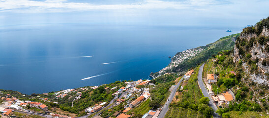 Aerial view of Amalfi, Italy, featuring cliffs with greenery, terraced vineyards, winding roads, terracotta roofed buildings, and the Tyrrhenian Sea.