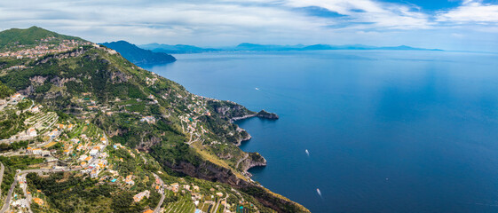 Obraz premium Aerial view of the Amalfi Coast in Italy, showing steep cliffs, terraced hills, colorful hillside villages, lush greenery, and the Tyrrhenian Sea with boats.