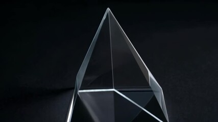 Crystal clear pyramid slowly rotating on black background, creating beautiful light refractions and reflections in studio environment - Powered by Adobe