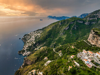 Aerial view of Amalfi town on Italy's Amalfi Coast, featuring cliffs, green hills, whitewashed buildings, a luxury hotel, and boats on the Tyrrhenian Sea. © Aerial Film Studio
