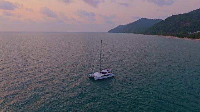 Peaceful sea cradles anchored sailboat near lush coast, Thailand. Aerial drone video