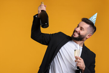Happy Birthday. Handsome man with party hat and champagne on orange background, space for text