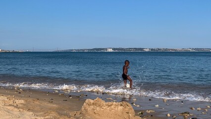 A joyful young Black boy gleefully dances in the foamy waves, evoking seaside revels and World...