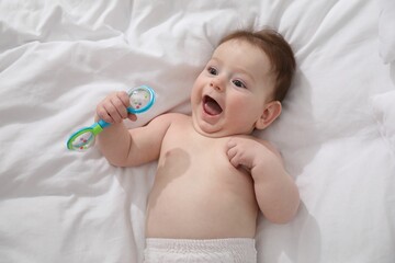 Cute little baby with rattle toy on bed at home, above view