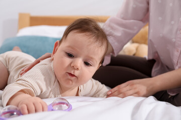Mother and her cute little baby with rattle toy on bed at home, closeup