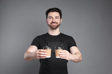 Portrait of smiling barista with paper takeaway cups of hot drink on grey background
