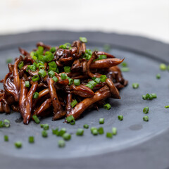 Shimeji mushroom served with chives on black stone plate. Typical oriental meal. Detail of food dish, closeup, selective focus.