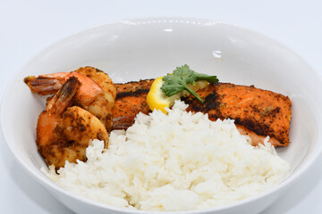 This image showcases a delicious meal featuring grilled shrimp, a perfectly seared salmon fillet topped with a fresh lemon slice and cilantro, accompanied by a serving of fluffy white rice.