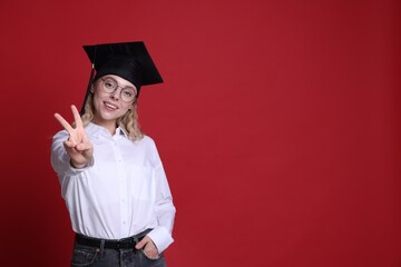 Happy student showing peace sign after graduation on red background. Space for text