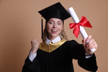 Happy student with diploma after graduation on beige background, selective focus
