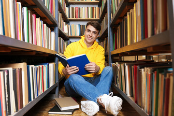 Man reading book near shelves in public library
