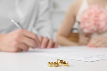 Newlyweds signing marriage contract and wedding rings on desk, selective focus