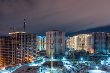 Construction site, cranes and multi-storey unfinished houses at night in winter