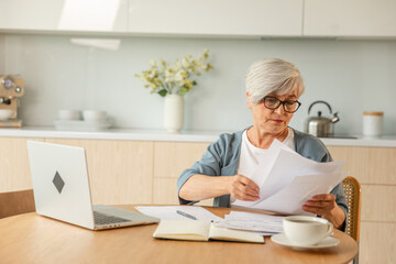 Middle aged senior woman sit with laptop and paper document, Pensive older mature lady reading paper bill pay online at home managing bank finances calculating taxes planning loan debt pension payment