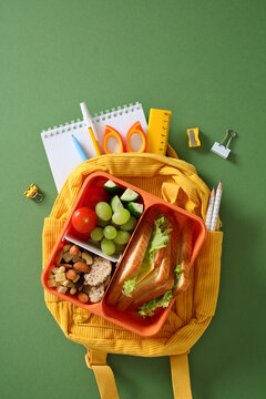 Healthy school lunchbox with sandwich, fruits, and nuts on yellow backpack on green background. Flat lay, top view.