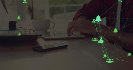 Two globes of digital icons spinning against mid section of a man using digital tablet at home