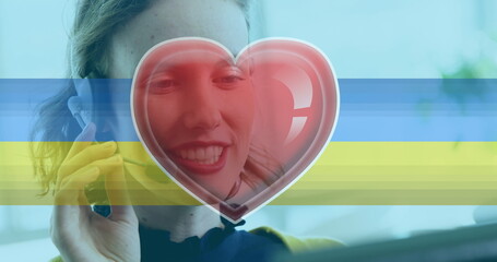 Image of heart icon and flag of ukraine with caucasian businesswoman using phone headset