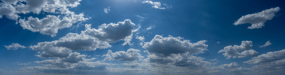 Panorama of a blue summer sky with fluffy white cumulus clouds a sun above the image
