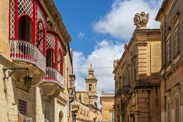 Mdina, Malta - 12.05.2025: The old city of Mdina with bright red window shutters and doors against traditional limestone houses, classic architecture of traditional medieval city in southern Europe.