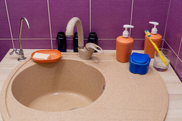 The bathroom sink is next to soap, shampoo, razor, toothbrush and
